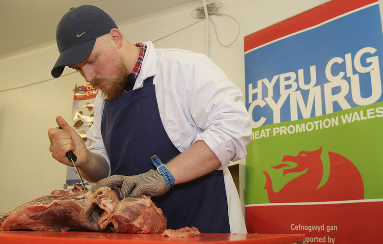 Butcher praparing meat in front of the HCC logo